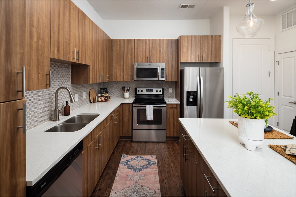 Dog-Friendly Apartments in Decatur, GA - Arlo Decatur - Kitchen With Vinyl Plank Flooring, Area Rug, Stainless Steel Appliances, Quartz Countertops, Designer Tile Backsplash, Breakfast Bar, and Wood Tone Cabinets