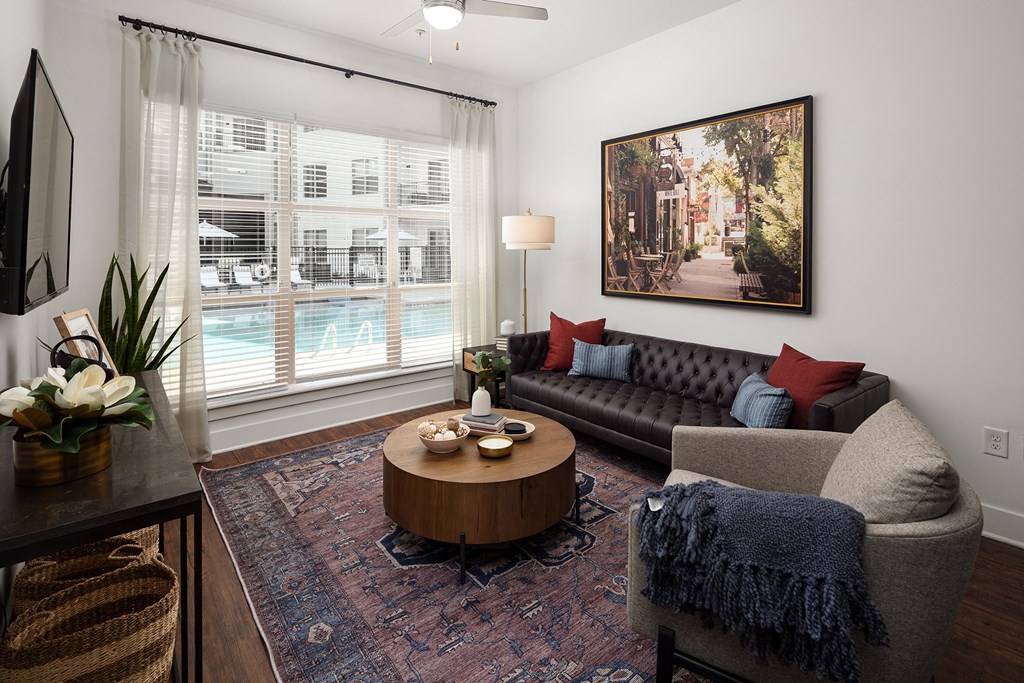 Apartments In Decatur, GA, For Rent - Arlo Decatur - Living Room With Vinyl Plank Flooring, Area Rug, Couch, Armchair, Round Coffee Table, Large Window With Blinds and Coverings, Ceiling Fan, Floor Lamp, Mounted TV, and Framed Wall Art