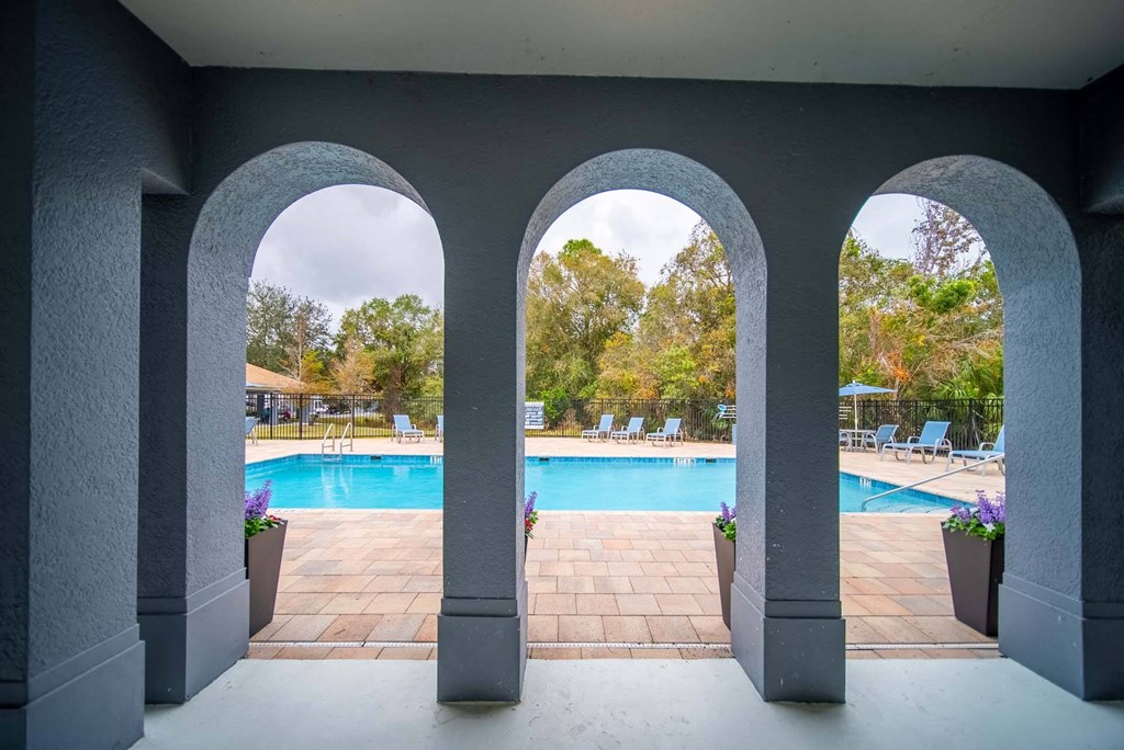 A pool area is seen through a window with three arches.
