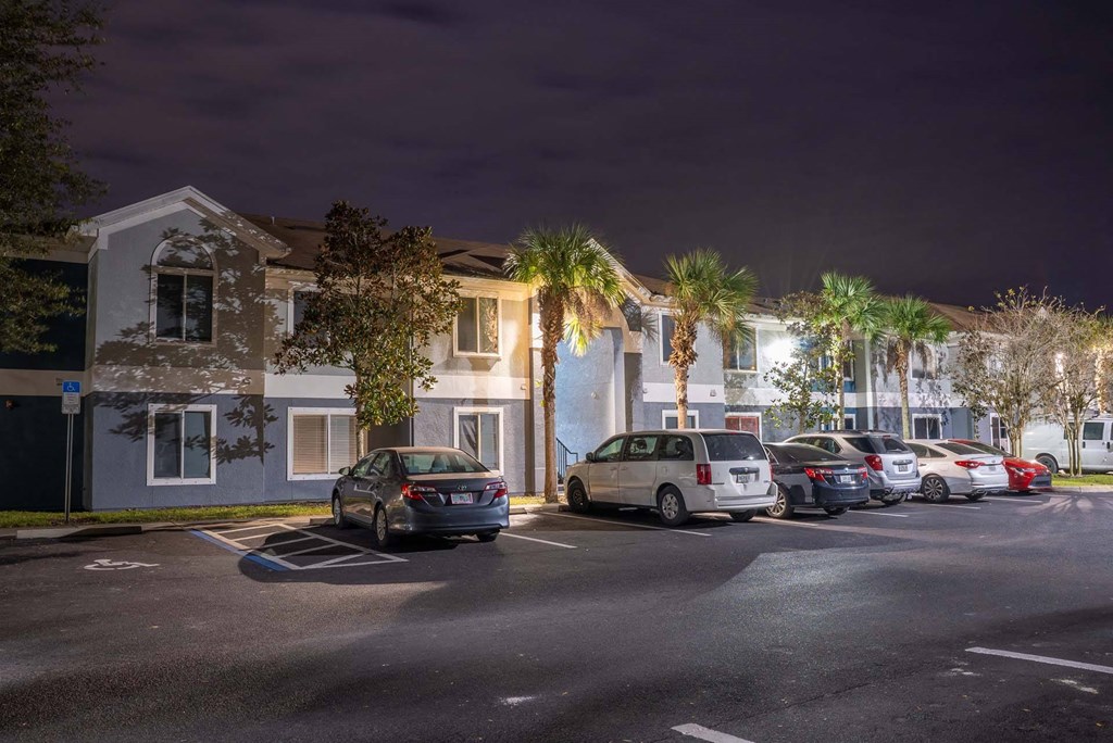 A parking lot with cars and a building with lights on in the background.