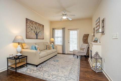 A living room with a beige couch, a chair, a table with a lamp, and a painting on the wall.