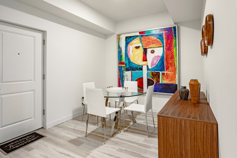 A dining room with a white table and chairs and a painting on the wall.