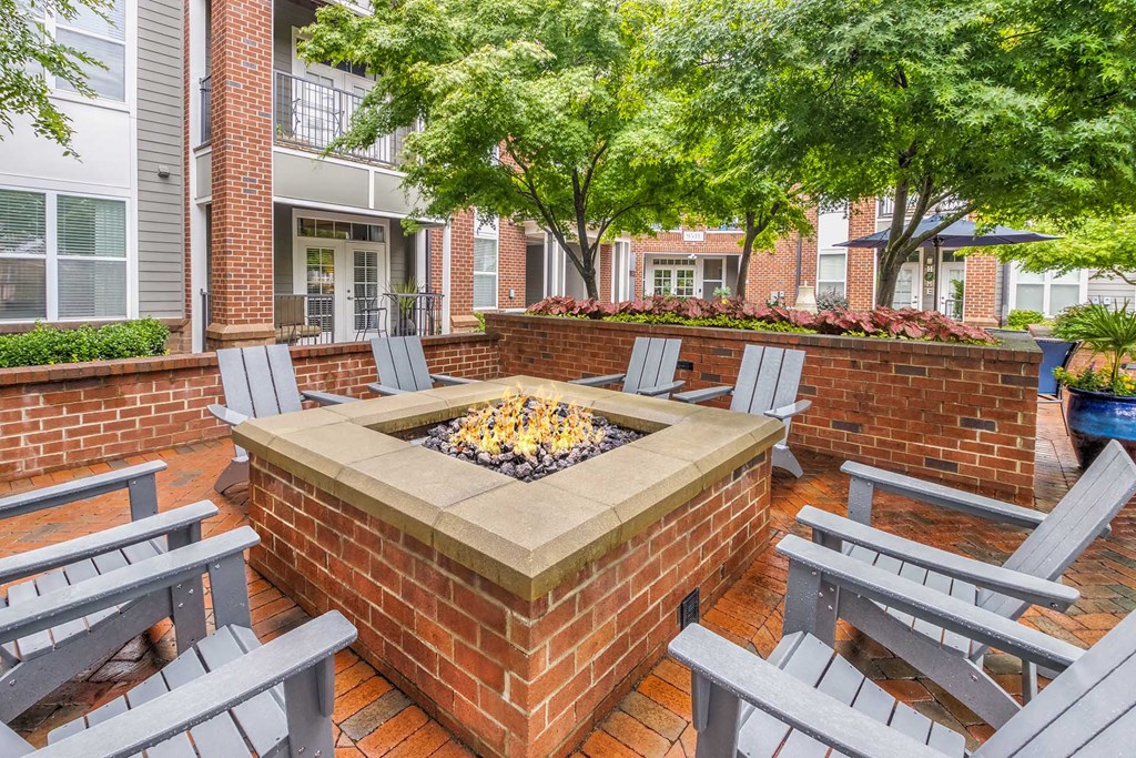 A brick fire pit is surrounded by grey chairs on a patio.