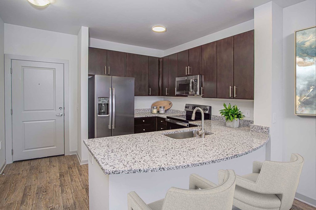 A kitchen with a granite countertop and two chairs.