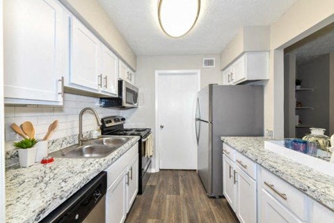 Lithonia, GA, Garden-Style Apartments Near I-20 - Woodcrest Village - Kitchen With White Cabinets, Stainless Steel Appliances, And Wood-Style Flooring.