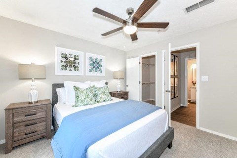 Lithonia, GA, Pet-Friendly Garden-Style Apartments - Woodcrest Village - Bedroom With A Ceiling Fan, Bedside Tables, Neutral Walls, and Carpet Flooring.