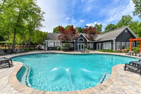 Lithonia, GA, Garden-Style Apartments Near Walmart Supercenter - Woodcrest Village - Swimming Pool With Lounge Chairs, Landscaped Trees, And A Clubhouse Building.
