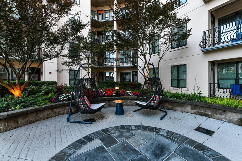 a courtyard with two swing chairs and a small table in front of an apartment building