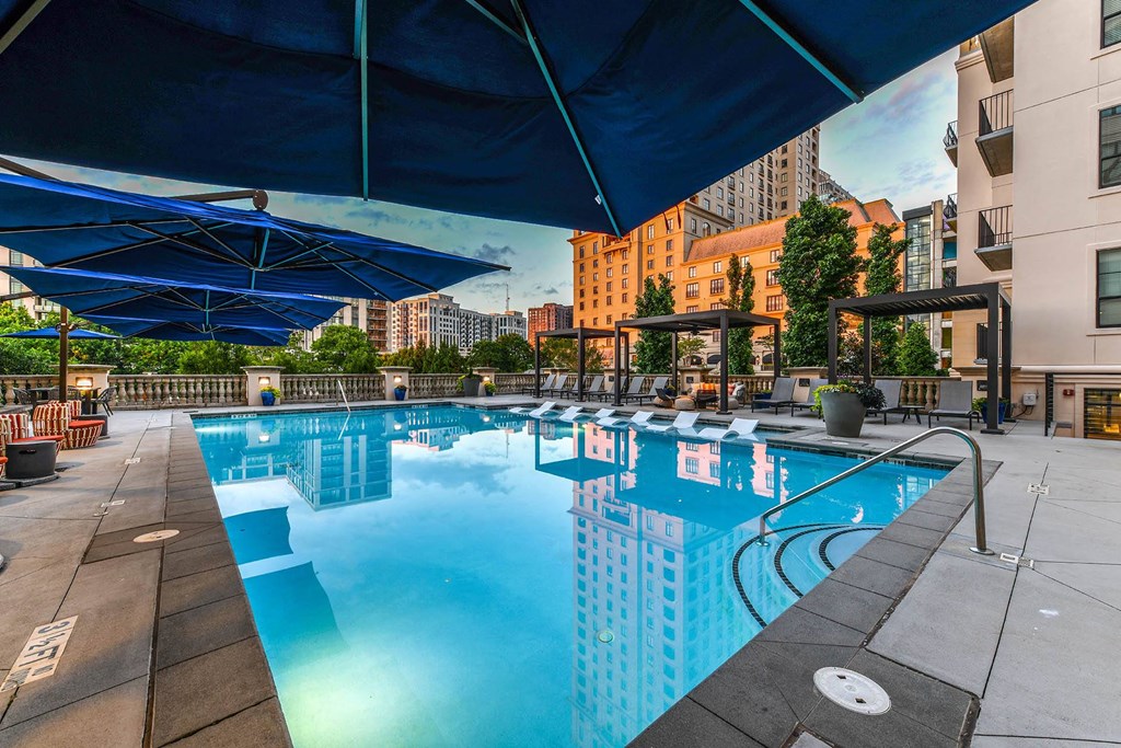 a swimming pool with lounge chairs and umbrellas in front of a building