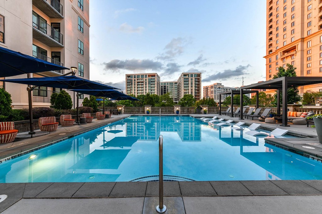 Luxury Apartments in Buckhead, GA, with In-Unit Washer and Dryer - 92 West Paces - Saltwater Pool with Submerged and Poolside Lounge Seats, Blue Umbrellas, Gazebos, Chairs, and Urban Views.