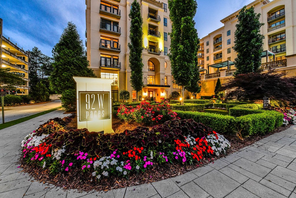 a sign in the middle of a flower garden in front of an apartment building