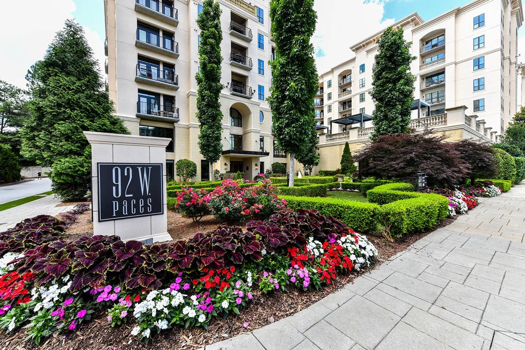 an apartment building with a sign and flowers in front of it