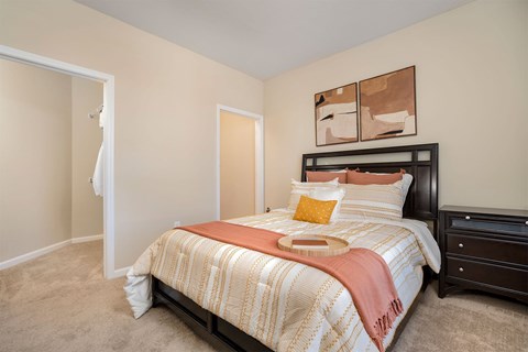 Apartments with Attached Garage in Cold Spring, KY - Brookstone Crossing - Bedroom with Carpet Flooring, Oversized Closet, Wall Art, Nightstand, and Bed.