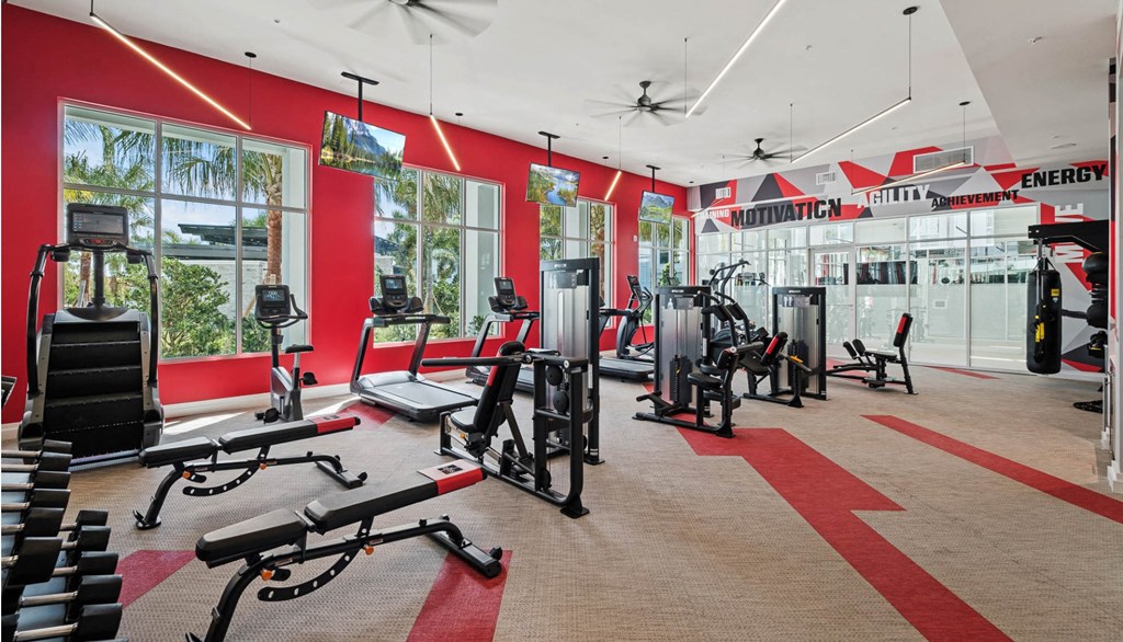a gym with cardio equipment and windows in a building with red walls