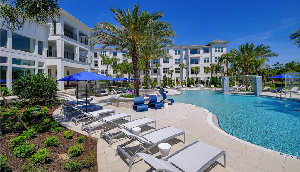 a swimming pool with lounge chairs and umbrellas in front of an apartment building