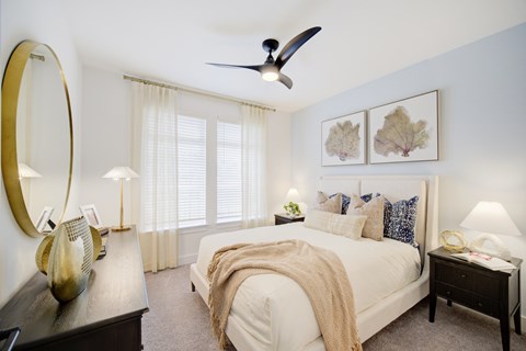 Panama City Beach, FL, Apartments with In-Unit Washer and Dryer - Vintage Lake Powell - Bedroom With White Bed, Layered Pillows, Two Nightstands With Lamps, Ceiling Fan, And Sheer Curtains.