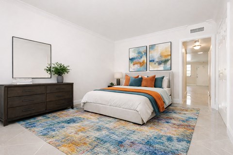 Three-Bedroom Luxury Apartments In Hollywood, FL - Park Hill Hollywood - A Bright, Modern Bedroom Featuring A Colorful Abstract Rug, Burnt Orange And Teal Bedding, And A Dark Wood Dresser.