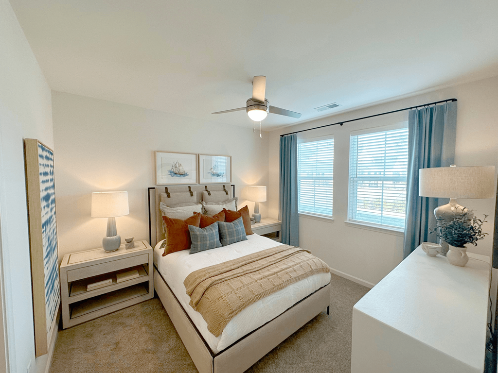 A bedroom with a large bed, a ceiling fan, and a window with blue curtains.