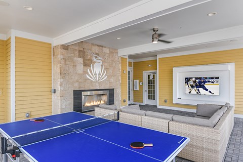 A blue ping pong table is in the middle of a living room with a fireplace and a painting on the wall.