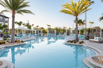 A large outdoor swimming pool surrounded by palm trees and lounge chairs.