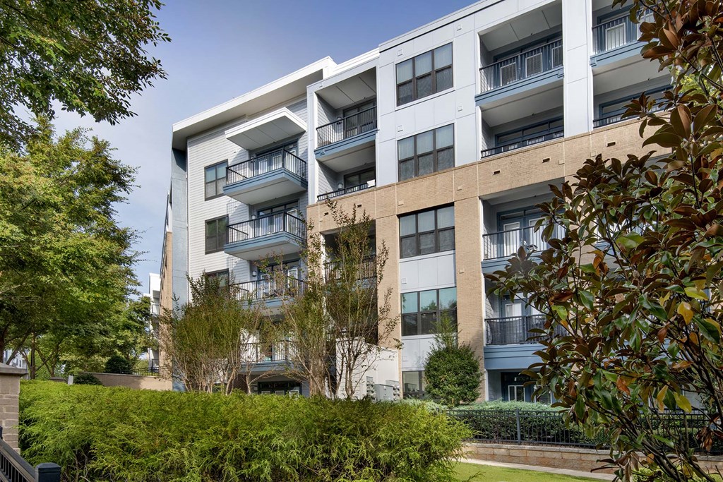 A modern apartment building with balconies and trees in the foreground.