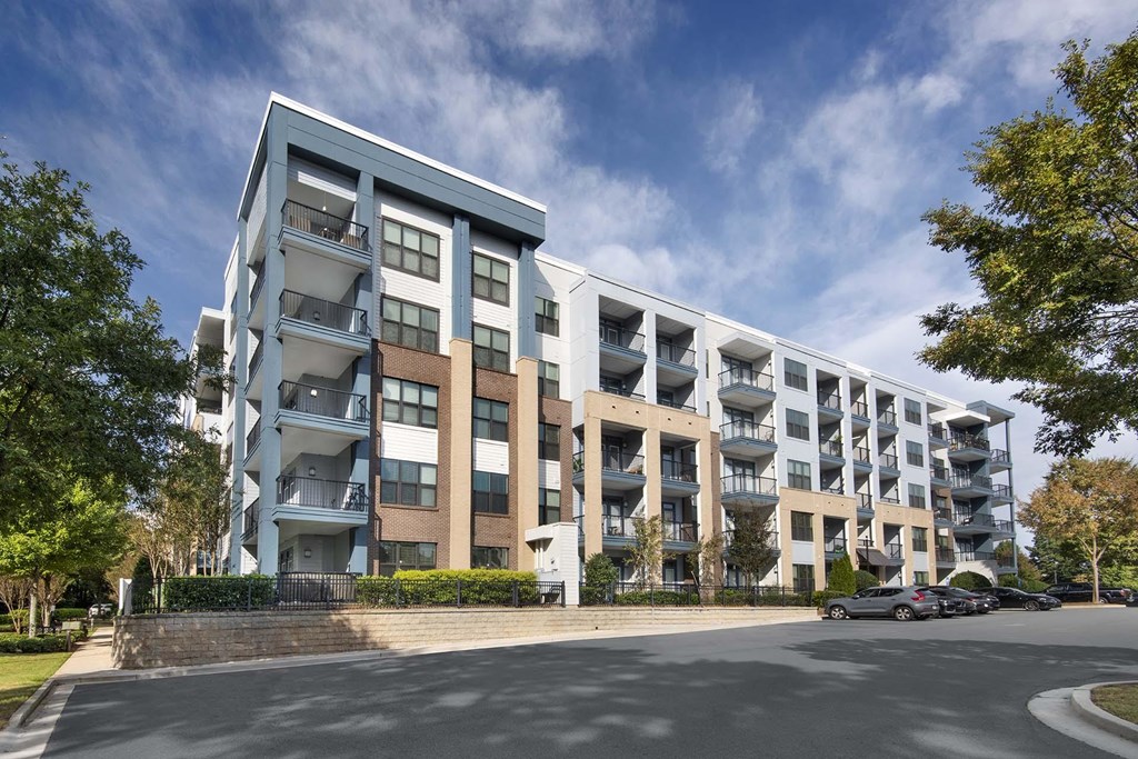 A modern apartment building with balconies and a parking lot in front.