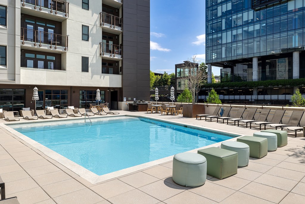 A swimming pool surrounded by lounge chairs and apartment buildings.