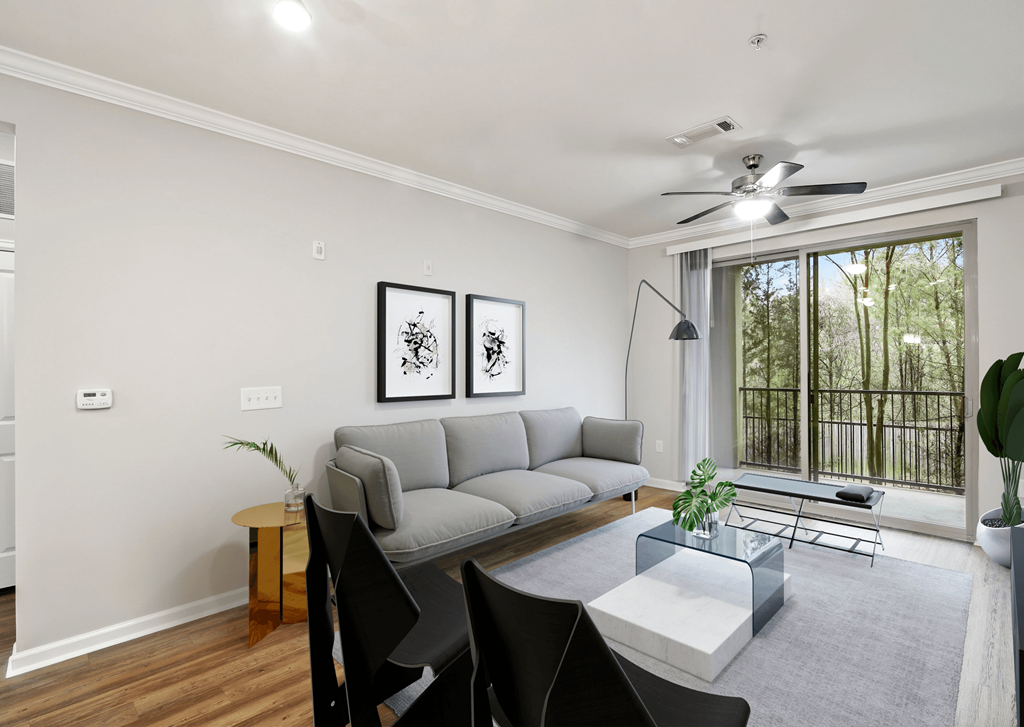 A living room with a grey couch, a glass table, and a ceiling fan.