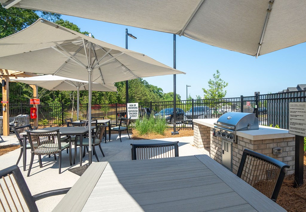 a patio with tables and chairs and a grill and umbrellas
