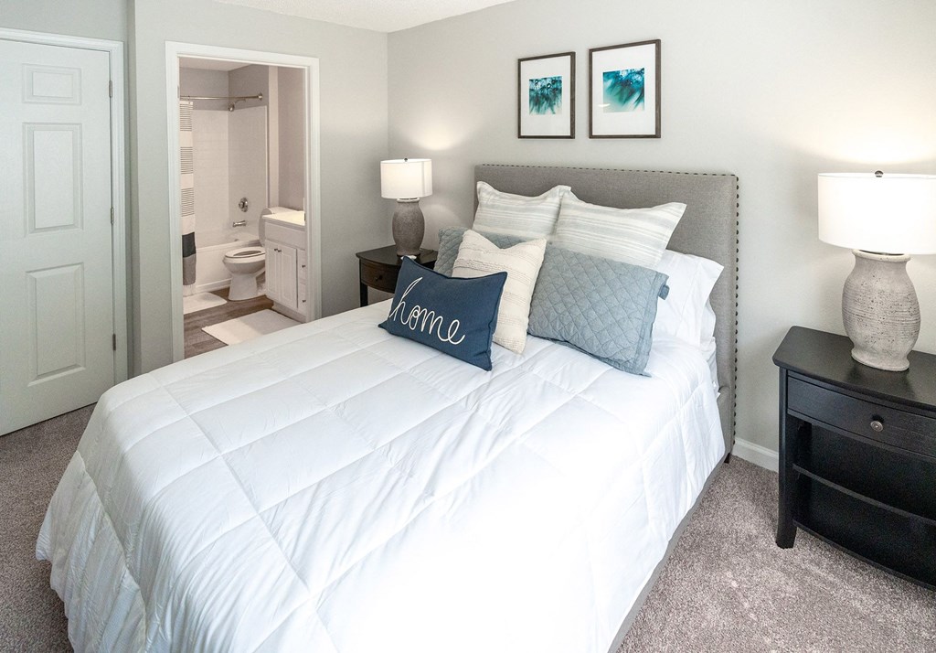 a bedroom with a white bed and pillows and a bathroom