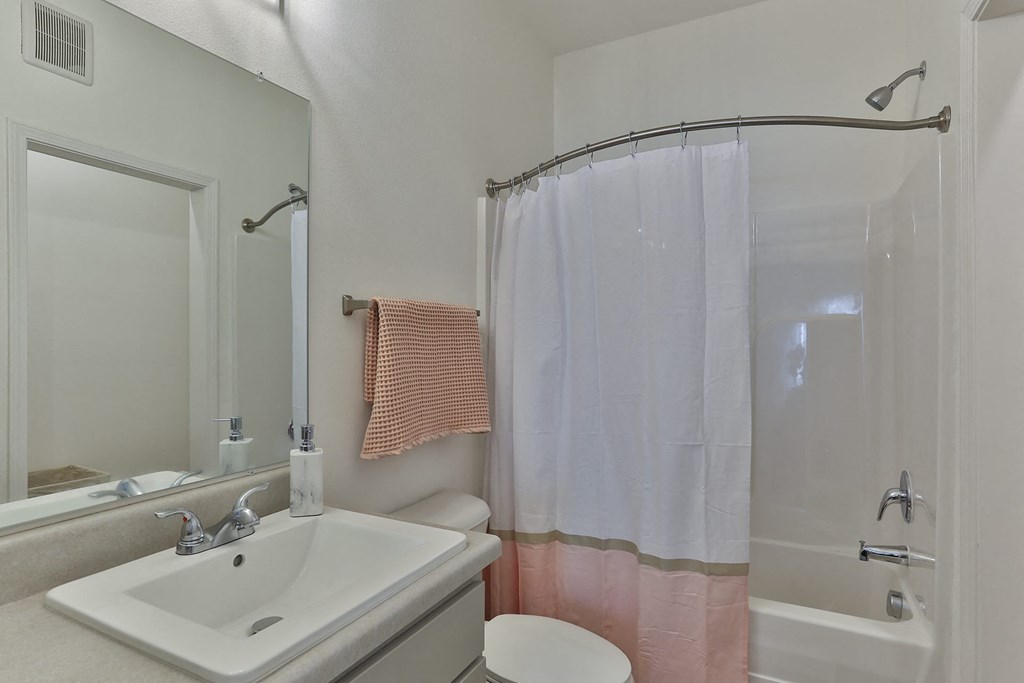 A white sink with a pink towel hanging on the shower curtain.