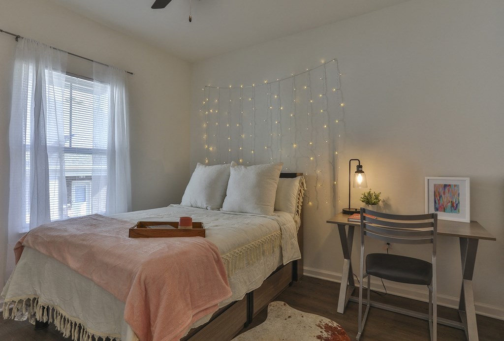 A bedroom with a bed, desk, chair, and ceiling fan.