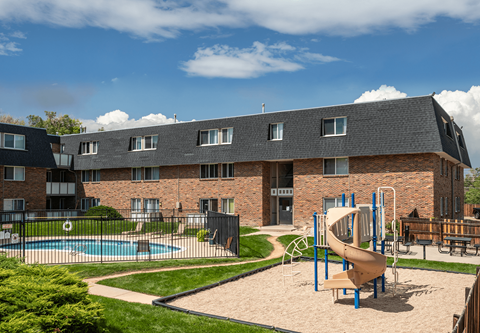 A playground with a slide and swimming pool in front of a brick building.