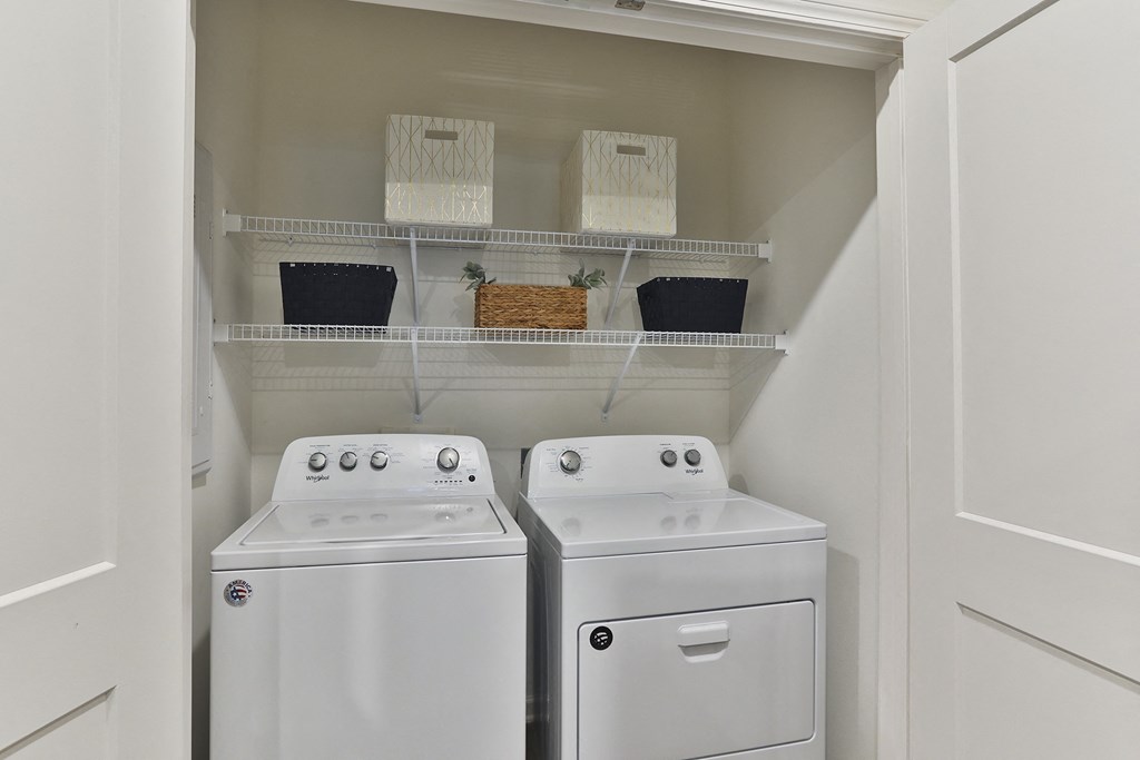 A white laundry room with two washing machines and shelves above them.