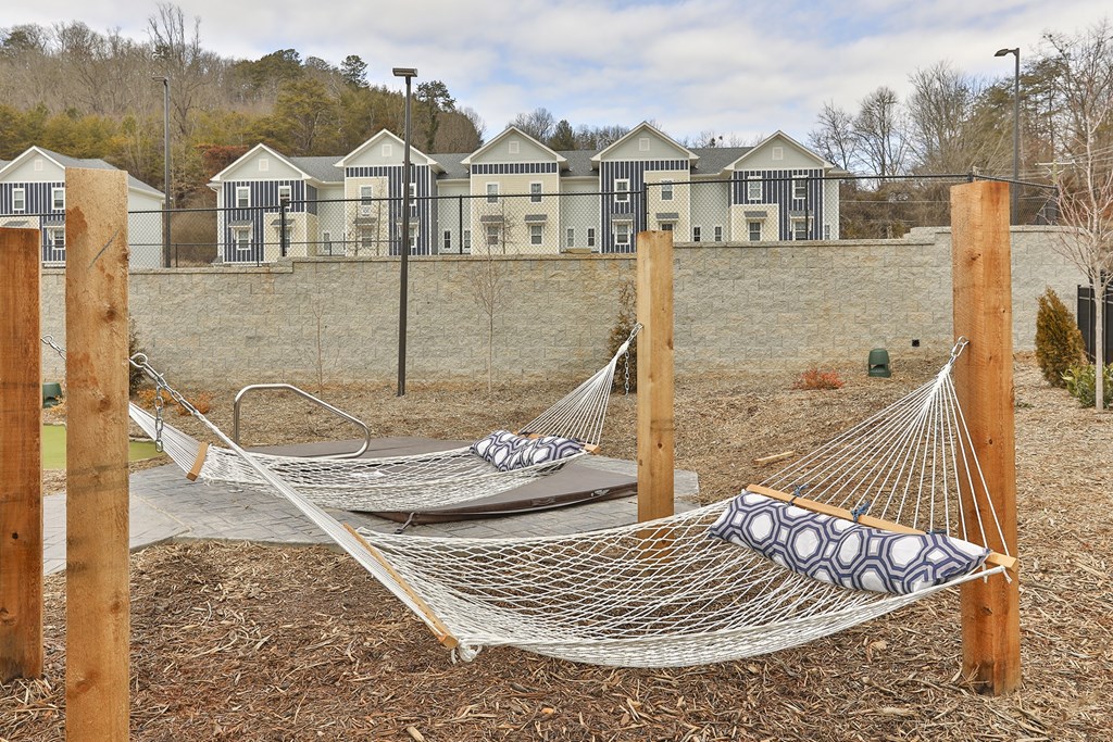 Two hammocks are strung between wooden posts in a yard.