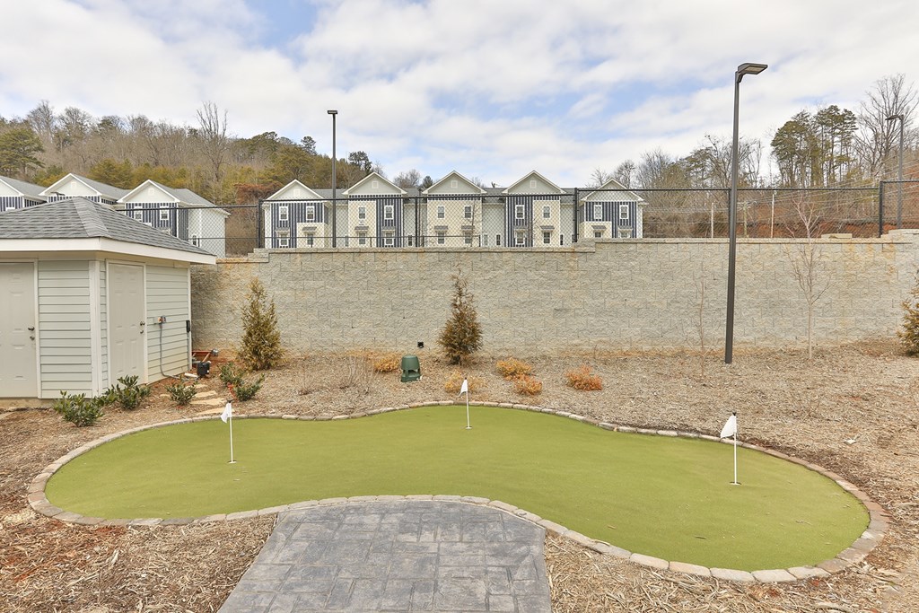 A small putting green in front of a wall of houses.