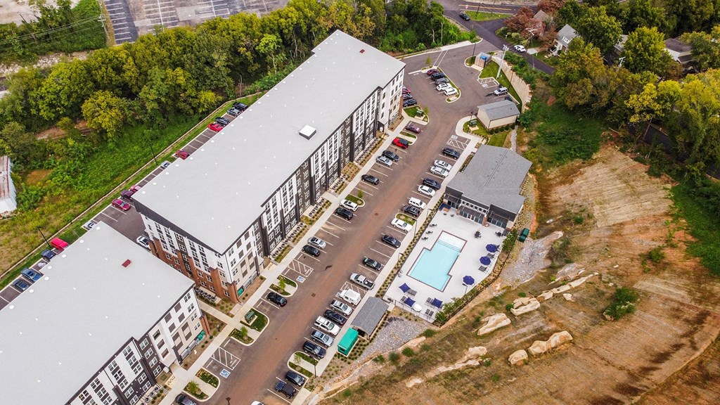 An aerial view of a parking lot with cars and a building with a pool.