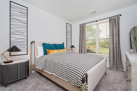 Wyoming, MI, Apartments with In-Unit Washer and Dryer - The Retreat Apartments - Bedroom With Upholstered Bed, Colorful Accent Pillows, Large Window, Gray Curtains, And Soft Carpet Flooring.