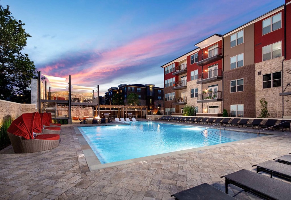 an outdoor swimming pool at dusk with an apartment building in the background