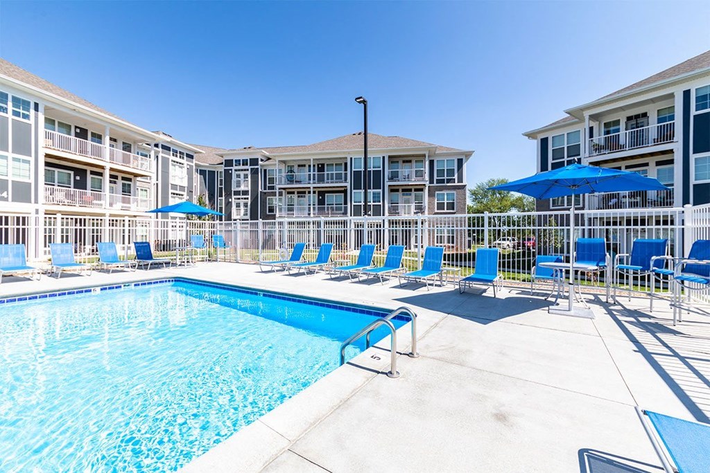 Pet-Friendly Apartments in Alexandria, KY - Elevation Apartment Homes - Outdoor Swimming Pool Surrounded by Fence, Blue Loungers, Umbrellas, and Apartments.