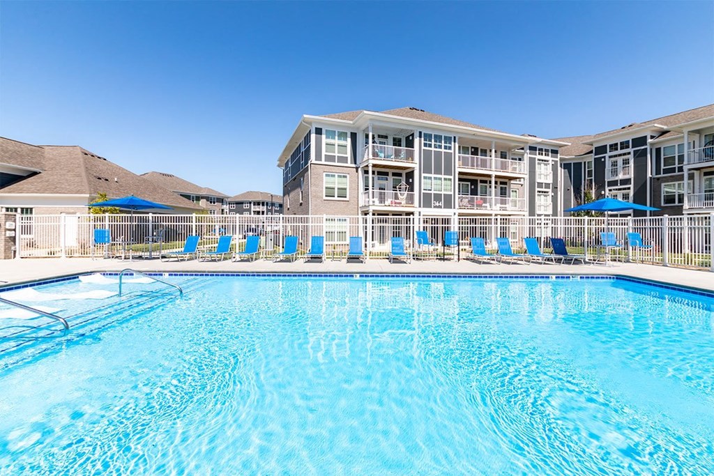 A large swimming pool in front of a multi-story building with sun loungers and umbrellas.