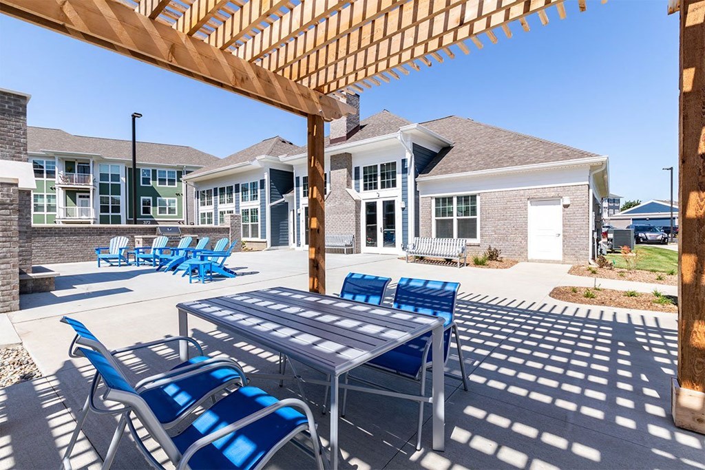 Dog-Friendly Apartments in Alexandria, KY - Elevation Apartment Homes - Outdoor Dining Area Under a Wooden Pergola with Table and Chairs, Overlooking the Clubhouse, Apartments, and Outdoor Lounge with Fire Pit and Lounge Chairs.