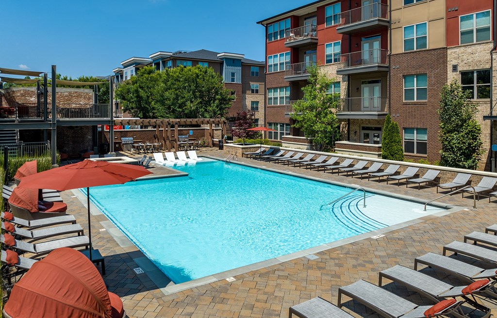 a swimming pool with chairs and umbrellas in front of an apartment building
