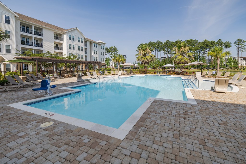 A large swimming pool surrounded by a brick patio and lounge chairs.