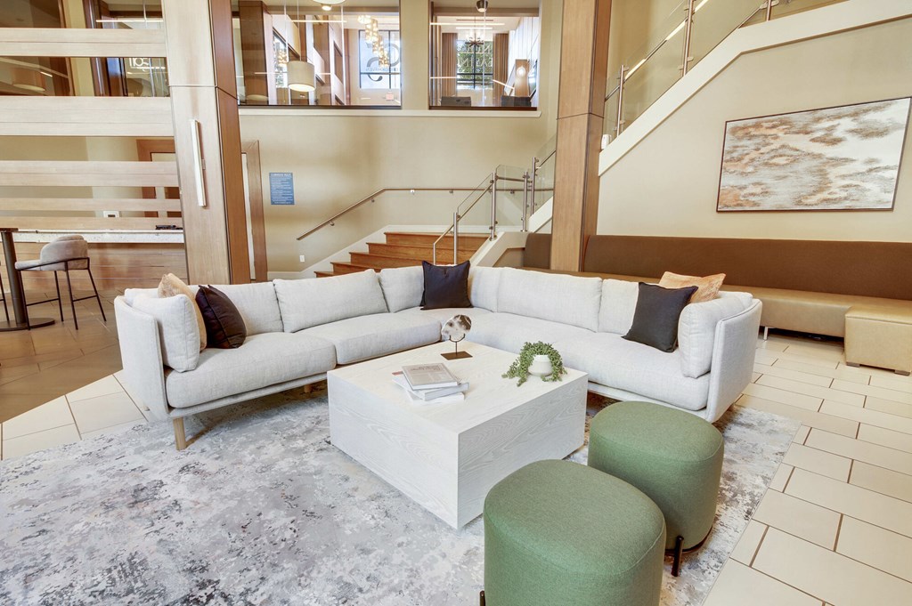 A white sofa with a green ottoman and a white coffee table in a spacious room.