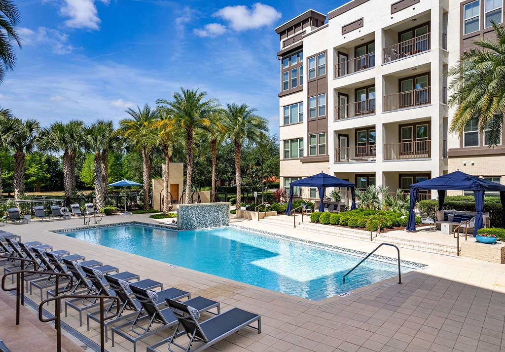 Pet-Friendly Apartments in Altamonte Springs FL - Nine12 Gateway - Sparkling Pool with Lounge Chairs, Navy Cabanas, Couches and Chairs, Landscaped Plants, Palm Trees, and View of Apartment Building