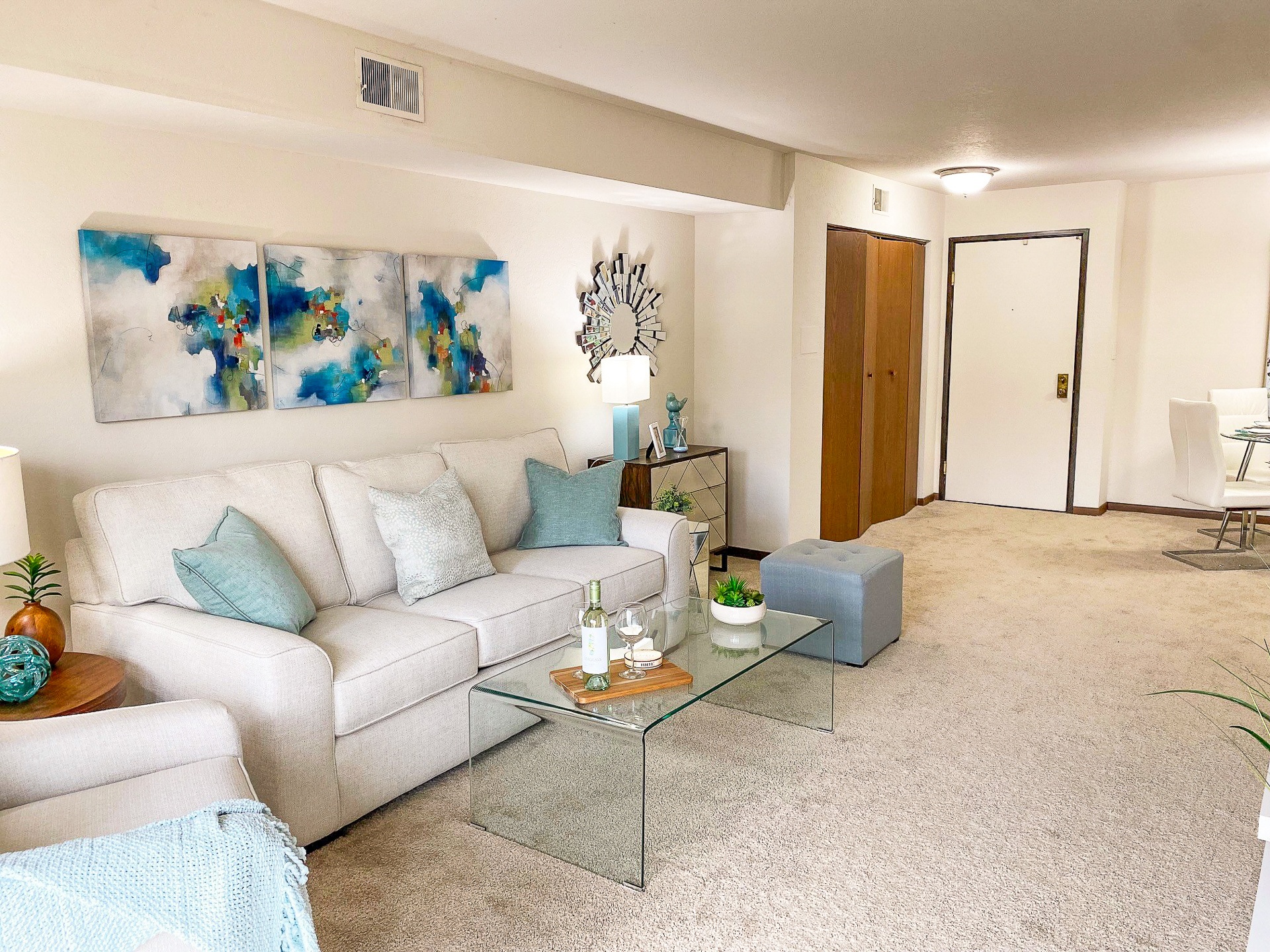 A living room with a white couch, a glass coffee table, and a painting on the wall.