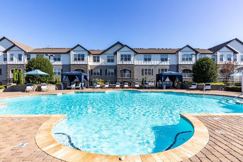 Two-Bedroom Luxury Apartments In Greenville, SC - The Aventine Greenville - A Large, Clear Blue Community Pool With Poolside Cabanas And Lounge Chairs In Front Of Stone-Accented Apartment Buildings.