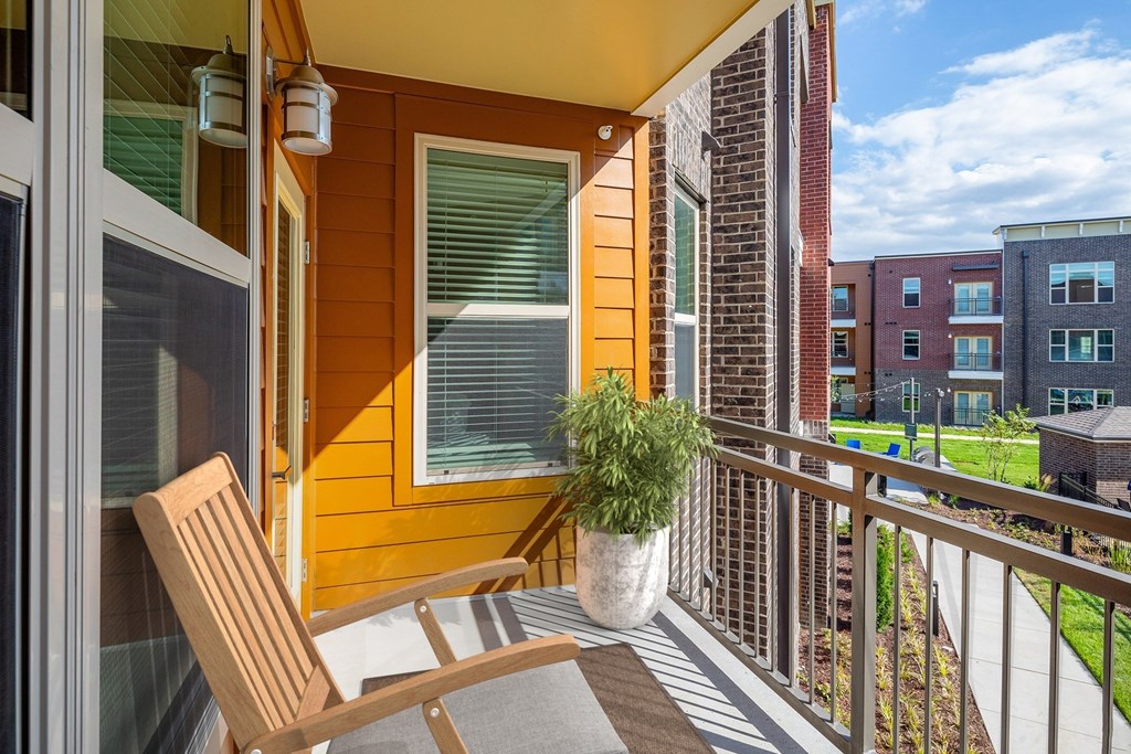 A balcony with a wooden chair and a potted plant.