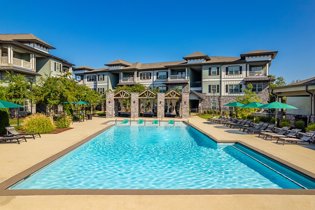 a swimming pool with chairs and umbrellas in front of an apartment building